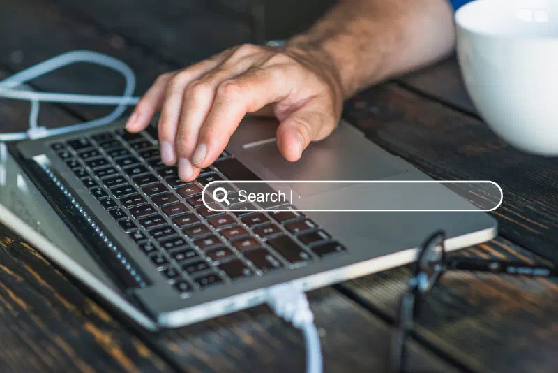 A hand typing on a laptop keyboard with a browser search bar graphic overlaid on the screen