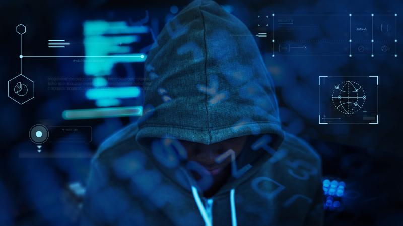 Hacker in a hoody working at computers in the dark